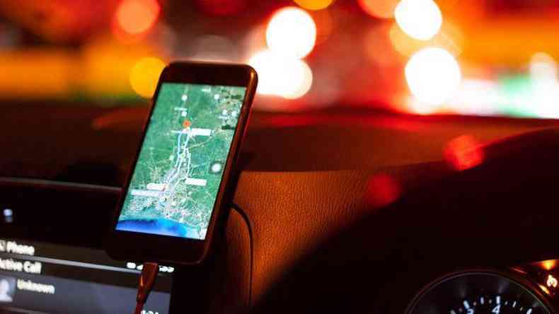 celular, apoiado em painel de um carro, com mapa de navegao aberto. ao fundo, luzes de trnsito