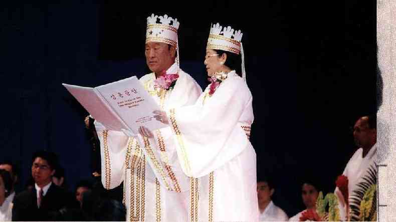 Um casal amarelo em roupas cerimoniais brancas em uma celebrao com pessoas em volta