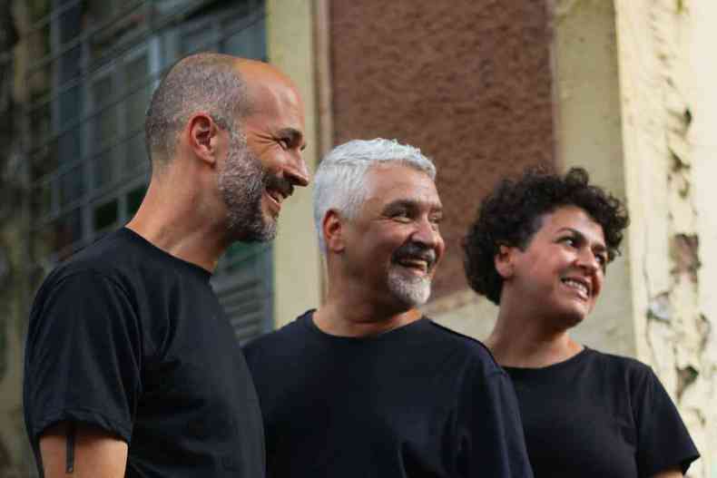 Vestindo camisetas pretas, os atores Marcel Luiz, Marco Túlio Zerlotini e Pauline Braga sorriem, olhando para o lado 