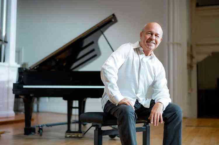 Pianista Enrique Graf sorri para a cmera e tem piano de cauda ao fundo