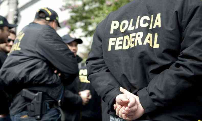 Agente da Polcia Federal de costas com as mos para trs. Ele usa jaquete preta e nas costas est escrito 'polcia federal'.