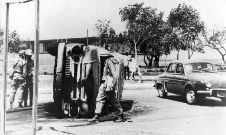 Imagem em preto e branco do perodo da Ditadura Militar no Brasil mostra militares analisando carro capotado.