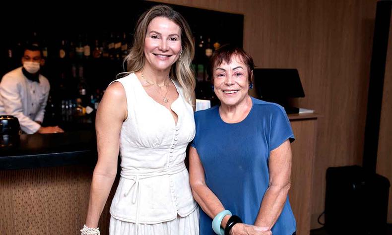 Rejane de Paula, de vestido branco, e Monica de Roure, de vestido azul, sorriem, olhando para a cmera 