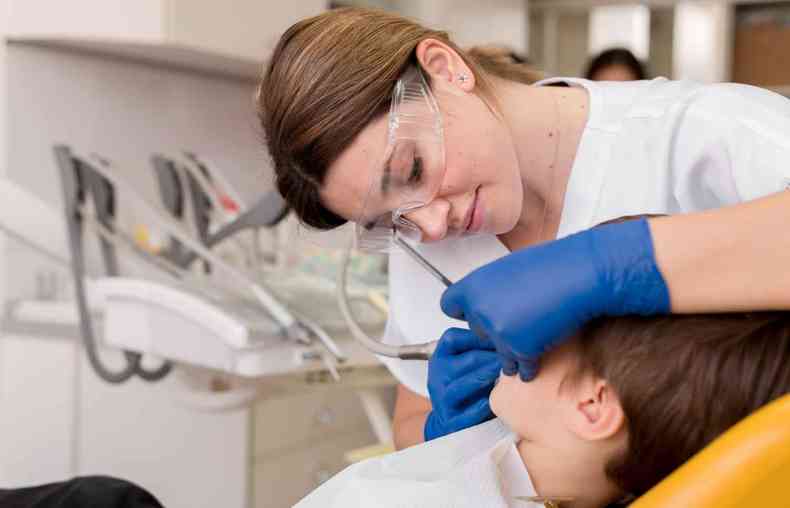 Dentista fazendo limpeza dentria em criana 