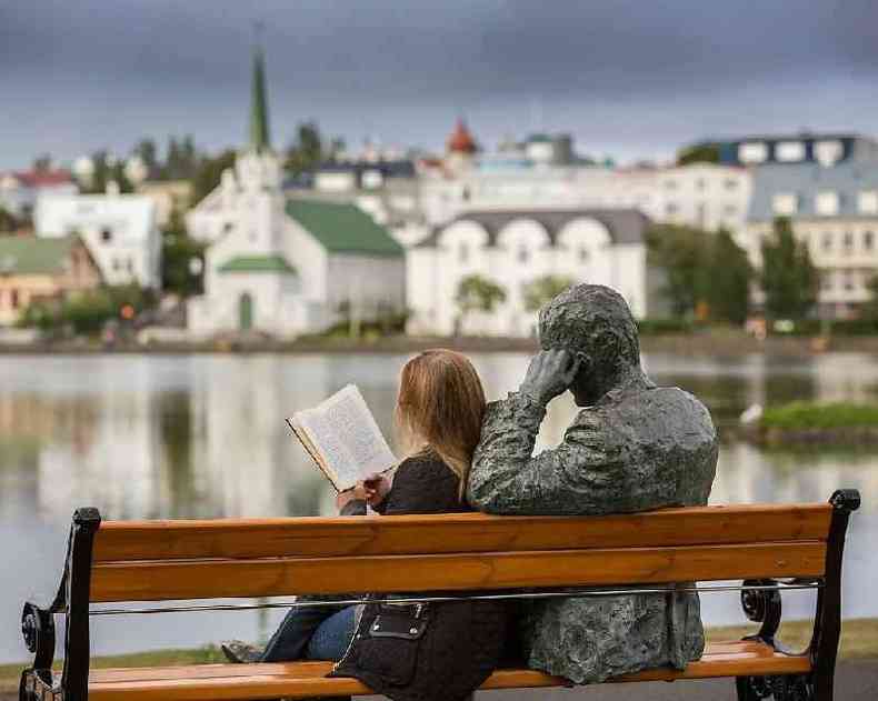 Mulher lendo ao lado de esttua do peta islands Tomas Gudmundsson em Reykjavik, Islandia.