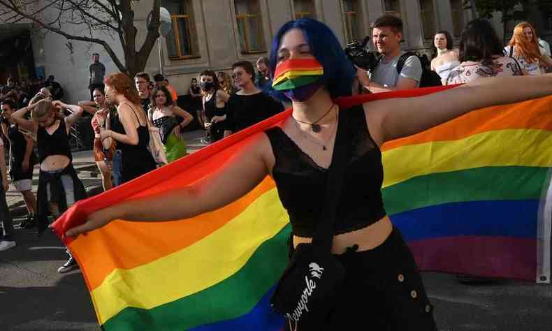 Imagem mostra mulher com mscara e bandeira com cores LGBTQIA em protesto 