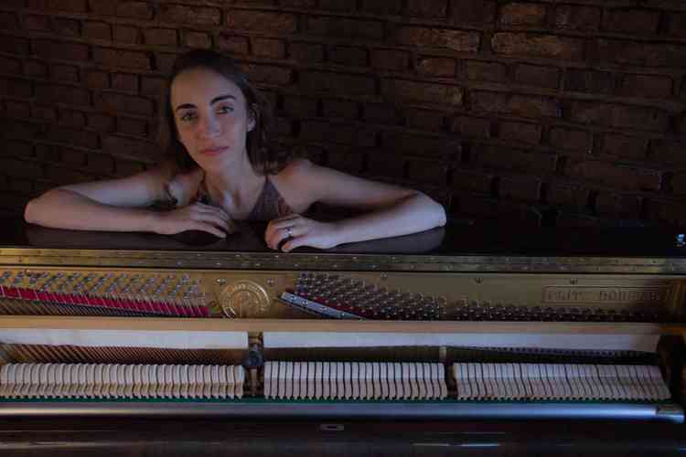 A pianista Lusa Mitre posa para foto com os braos apoiados em piano aberto
