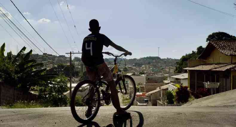 Menino anda de bicicleta com fundo de bairro da periferia