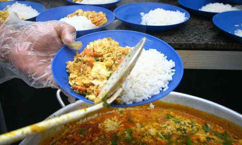 Imagem ilustrativa: pessoa serve prato de comida em refeitrio