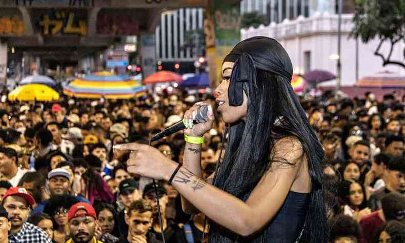 Vestindo preto e com microfone na mo, MC Colombiana se apresenta em palco em frente a pblico no Duelo de MCs