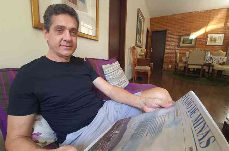 Marcelo Frattezi, homem branco com camisa preta, l o novo Estado de Minas sentado em um sof em sua casa