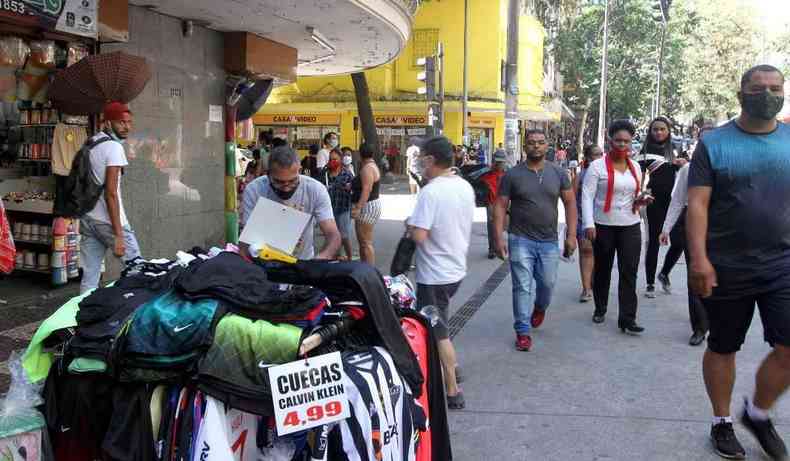 Pessoas caminham pelas caladas do Centro de Belo Horizonte, vendedor ambulante de cuecas em frente.