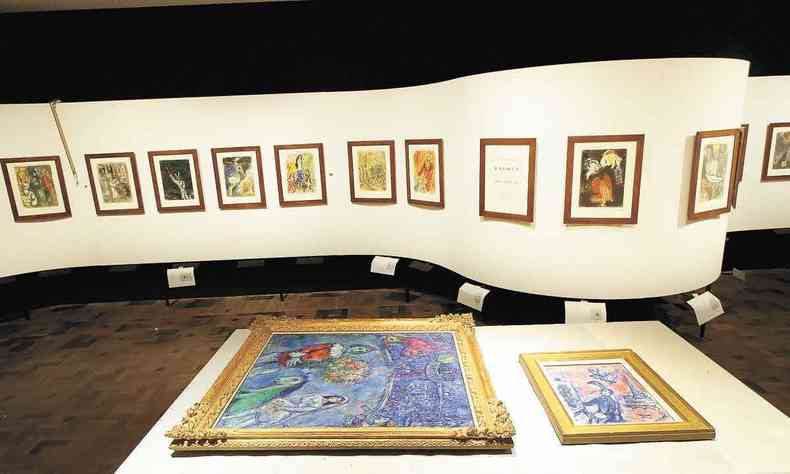 Quadro 'O galo violeta' está sobre a mesa. Ao fundo, veem-se pinturas de Marc Chagall penduradas em estrutura ondulada em uma das salas do CCBB, em Belo Horizonte