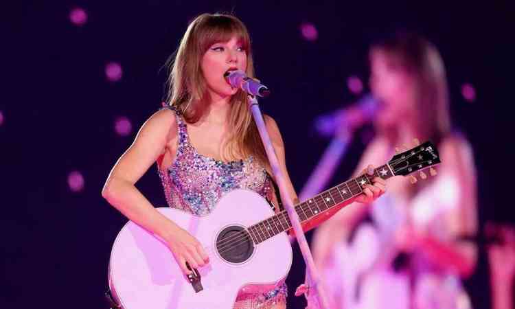 Taylor Swift canta ao microfone tocando um violo