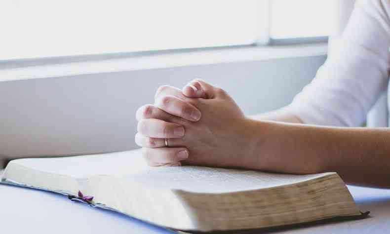 Pessoa reza com as mãos sobre uma bíblia
