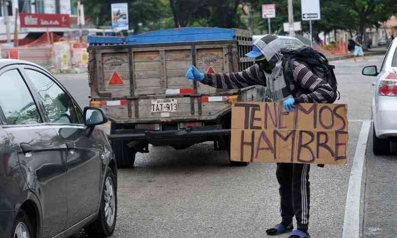 Migrante venezuelano pede esmola nas ruas de Guayaquil, no Equado, enquanto segura cartaz dizendo 
