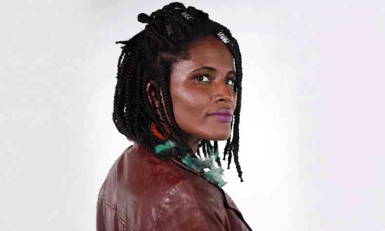 Djamila Ribeiro, mulher negra com cabelos tranados na altura do ombro, usa jaqueta vermelho escuro e est posicionada de lado, com o rosto voltado para a cmera