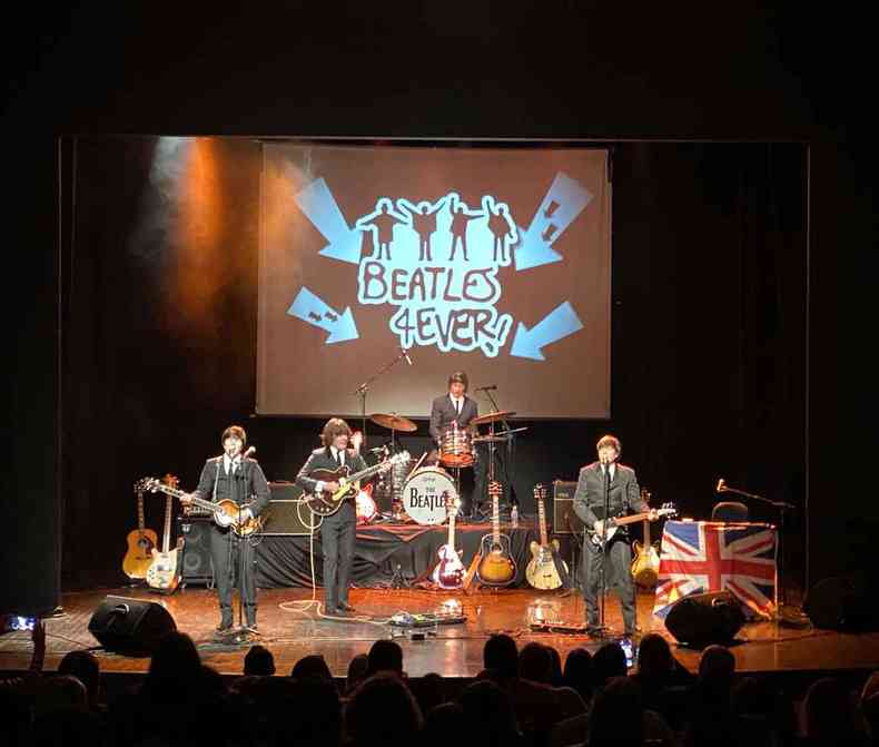 Banda brasileira Beatles 4Ever se apresenta no palco.  direita, est bandeira da Inglaterra . No alto, projeo traz o nome do grupo e ilustrao que remete aos Beatles