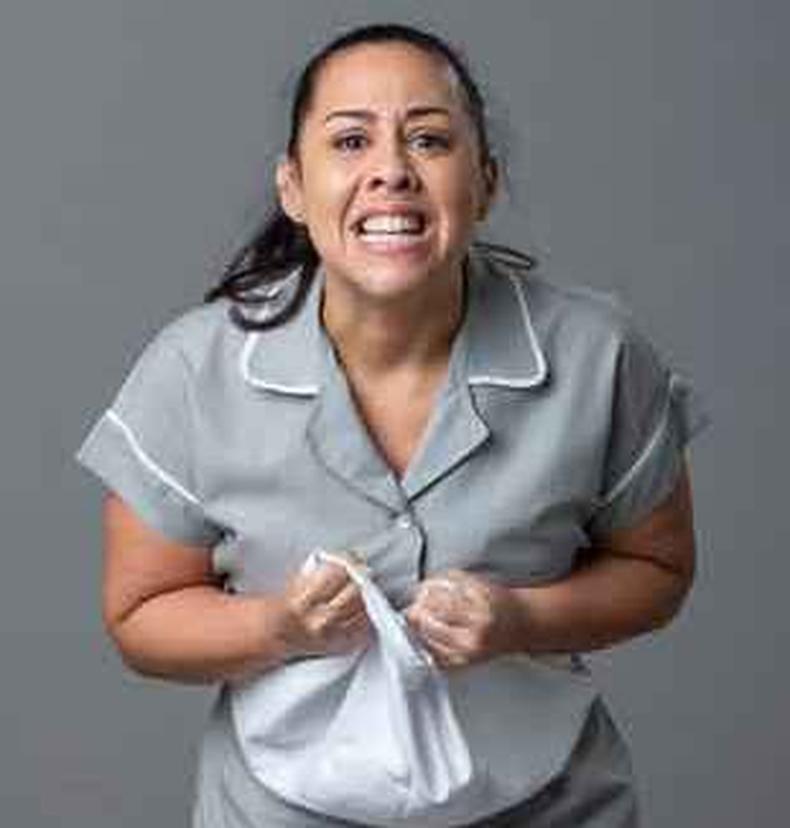Evelyn Castro usa uniforme de empregada e faz cara de raiva, apertando guarda-p, como a personagem Deusa
