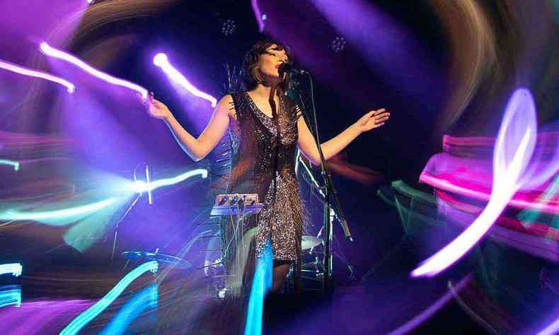 Com vestido preto, no palco, diante do microfone, a vocalista Salma J abre os braos e canta 
