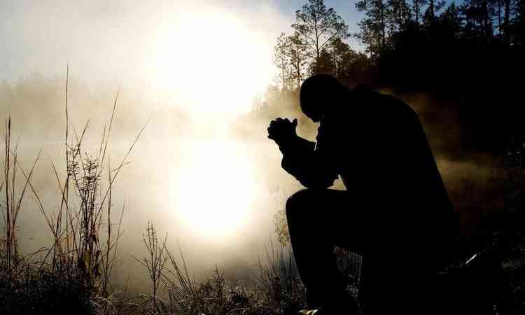 homem rezando ao ar livre, em meio  natureza
