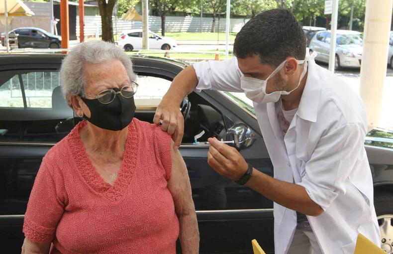 Idosa de blusa vermelha e mscara recebe vacina de um enfermeiro