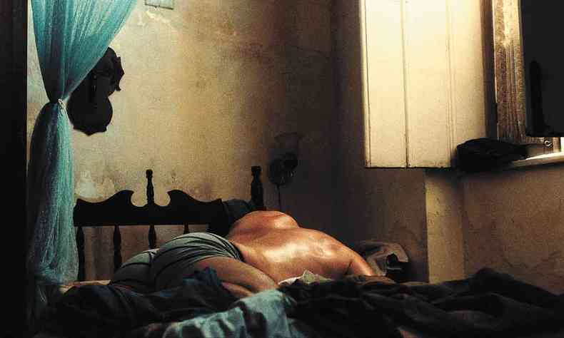 Homem deitado de costas em ambiente de penumbra em cena do filme Deserto particular