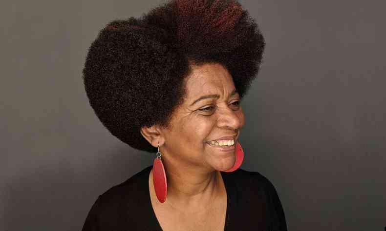 Maria da Conceição, mulher negra, Posando com cabelo estilo black power contra fundo cinza escuro 