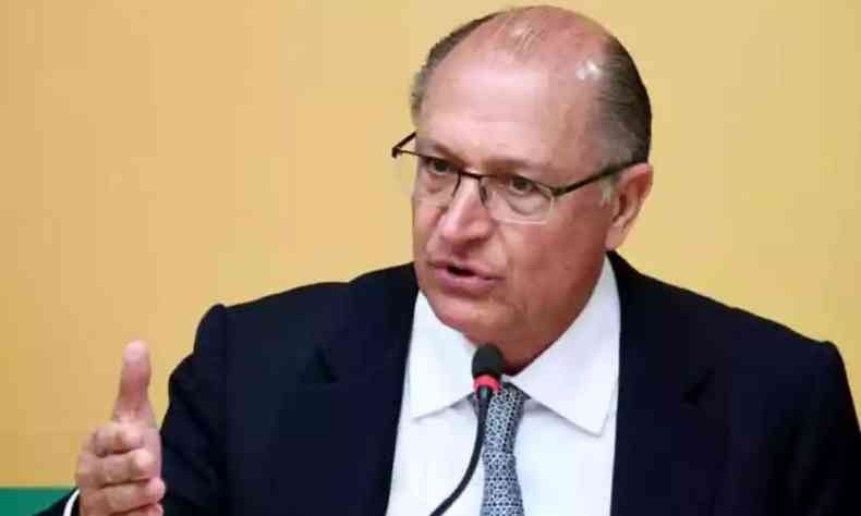 Geraldo Alckmin, sentado e de terno, gesticula com uma mo enquanto fala