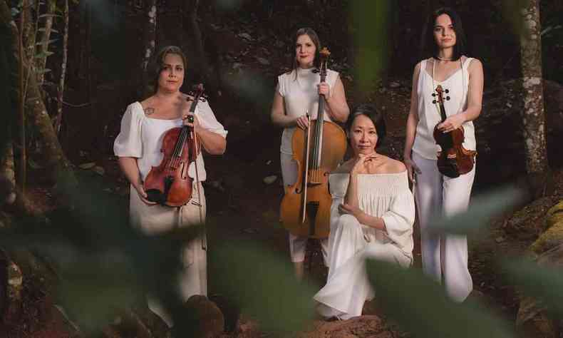 Quatro integrantes do quarteto boulanger vestem roupas brancas, seguram instrumentos musicais e posam para foto entre rvores e folhagens