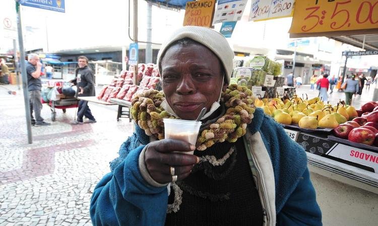 Uma pessoa com um copo na m�o, com roupas de frio. Ao fundo pode-se ver v�rias frutas.