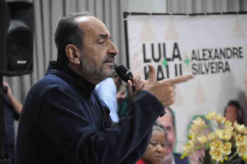 Alexandre Kalil fala ao microfone, no fundo um cartaz de campanha com os nomes de Kalil, Lula e do senador Alexandre Silveira
