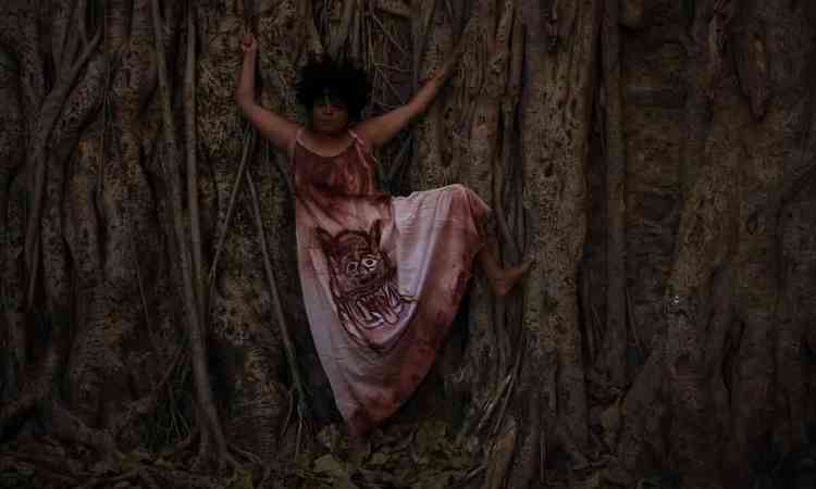 Cantora Priscila Magella posa, com os braos abertos, encostada em tronco de rvore gigantesco
