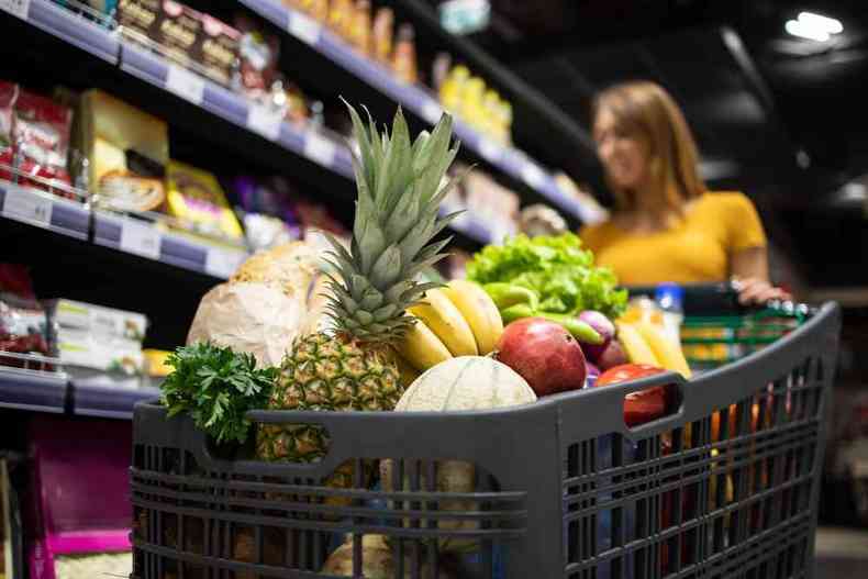 Mulher no supermercado com um carrinho cheio de frutas