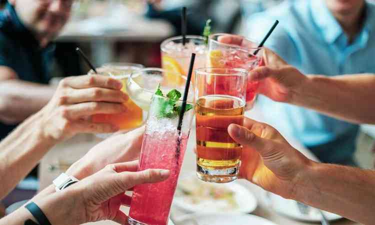 pessoas brindam com bebidas alcoolicas em uma mesa de bar