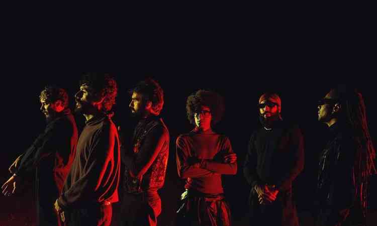 Seis integrantes da banda A Outra Banda da Lua, de perfil, no escuro
