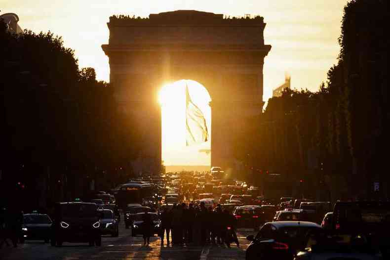 Arco do Triunfo, em Paris, no pôr do sol, observado por turistas na Champs Elysèes
