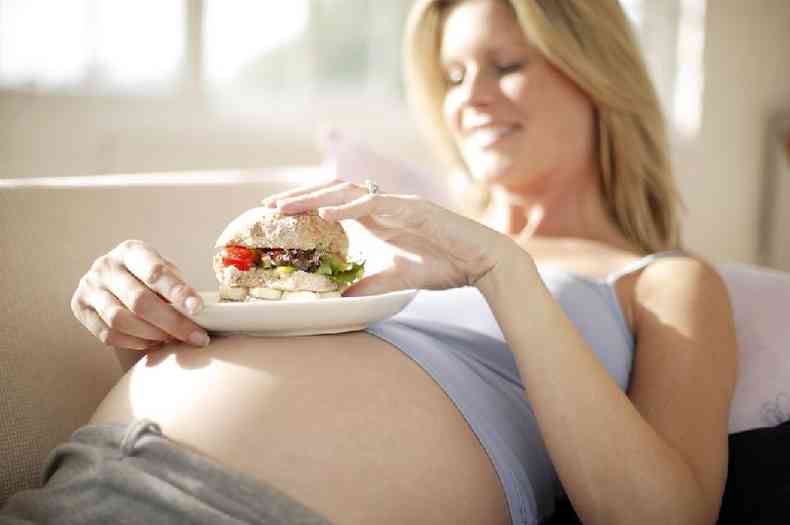 Mulher grávida comendo hamburguer