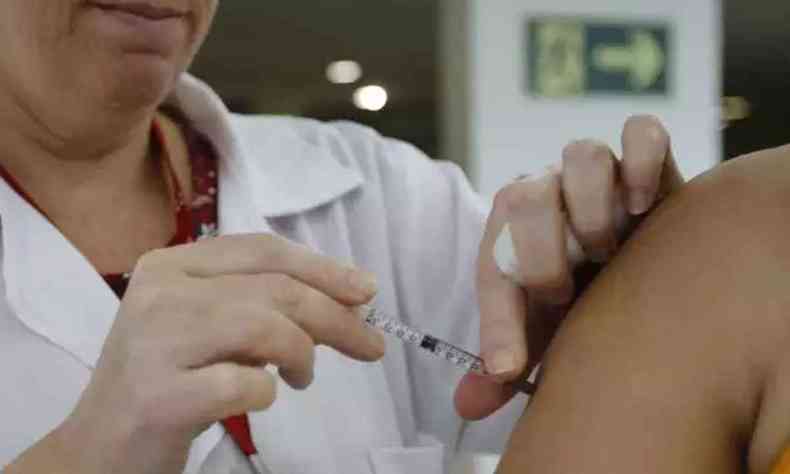 Na foto, enfermeira aplicando vacina da gripe no braço de uma mulher. 