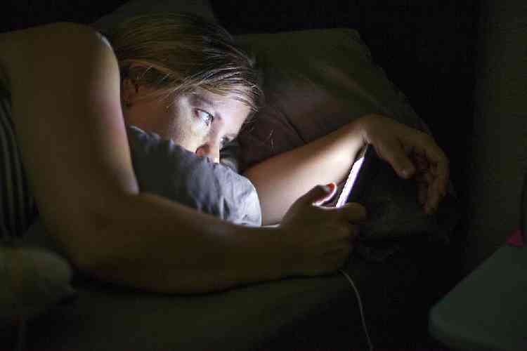 Mulher checando o celular  noite na cama 