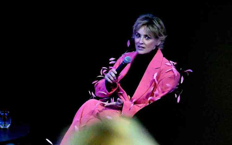 Sharon Stone veste terno rosa e segura um microfone 