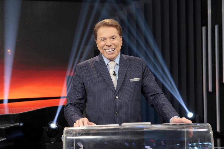 O apresentador Silvio Santos sorri enquanto usa um terno preto 