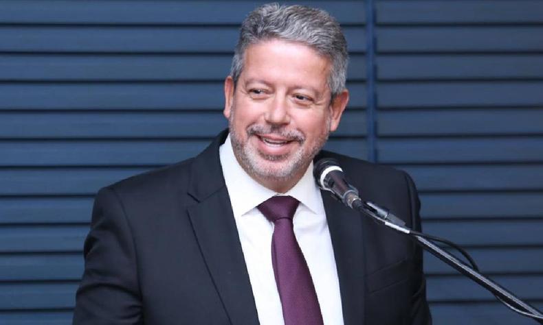Arthur Lira de terno preto, camisa branca e gravata bord falando ao microfone em um fundo azul escuro