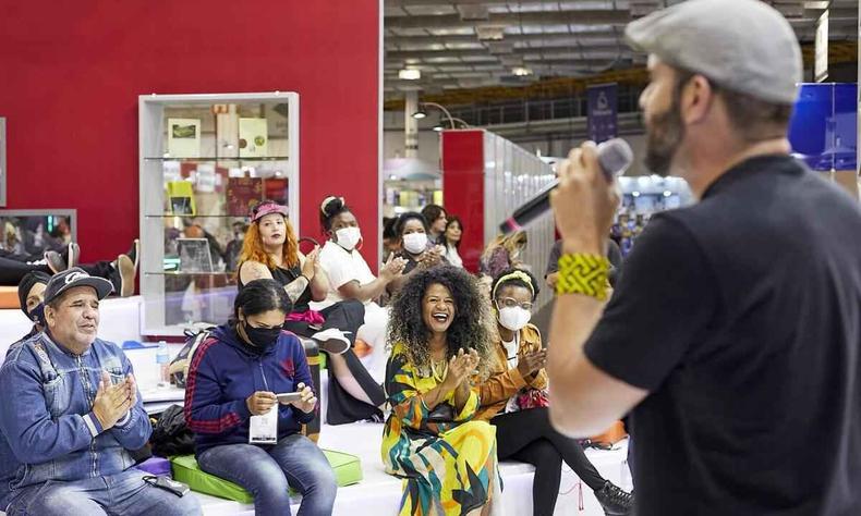 Leitores sentados sorriem enquanto homem conta histrias ao microfone na Bienal Internacional do Livro de So Paulo 