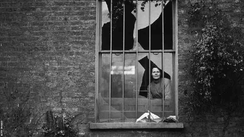Uma mulher observa através de uma janela quebrada no presídio feminino Holloway, em Londres, depois de um ataque a bomba em dezembro de 1913