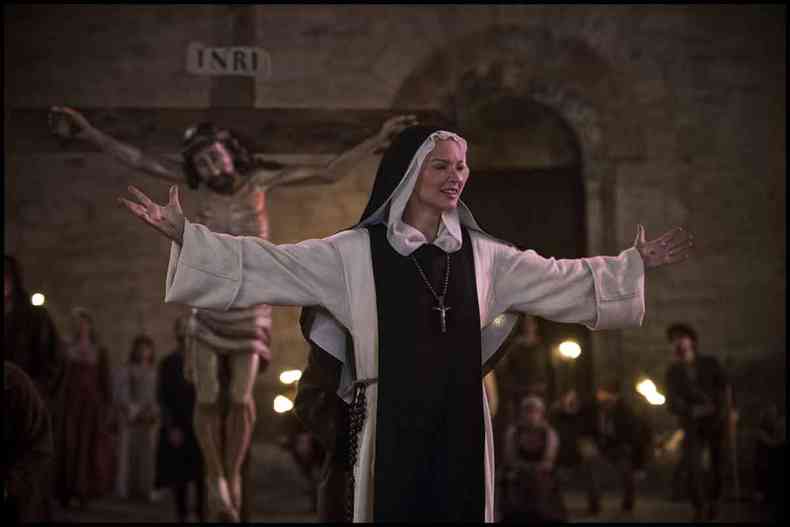 Virginie Efira interpreta a freira Benedetta, que está de braços abertos em frente a imagem de Jesus crucificado, em cena do filme Benedetta