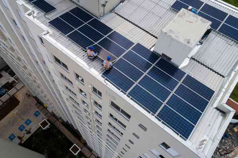 Operrios instalam painis solares em teto de edifcio