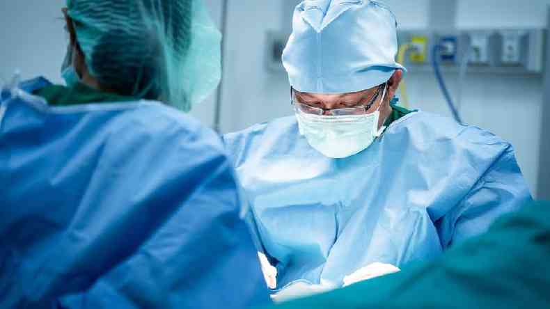 Um cirurgio usando culos e uma mscara facial  visto olhando para baixo durante uma operao