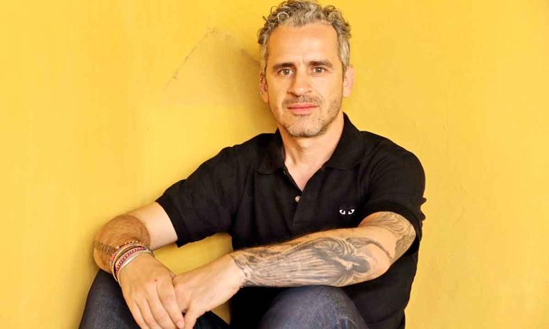 Jos Luis Peixoto vestido de preto e sentado no cho, com fundo de parede amarela