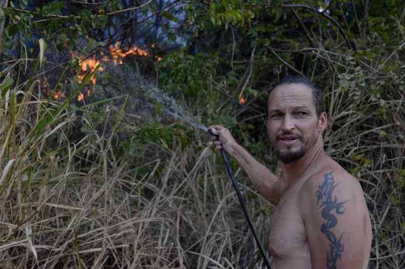 Imagem mostra Jos ao lado da vegetao segurando uma mangueira de jardim preta. Ele joga gua para apagar o fogo. Ele  um homem de 56 anos, com cavanhaque e uma tatuagem no brao esquerdo.